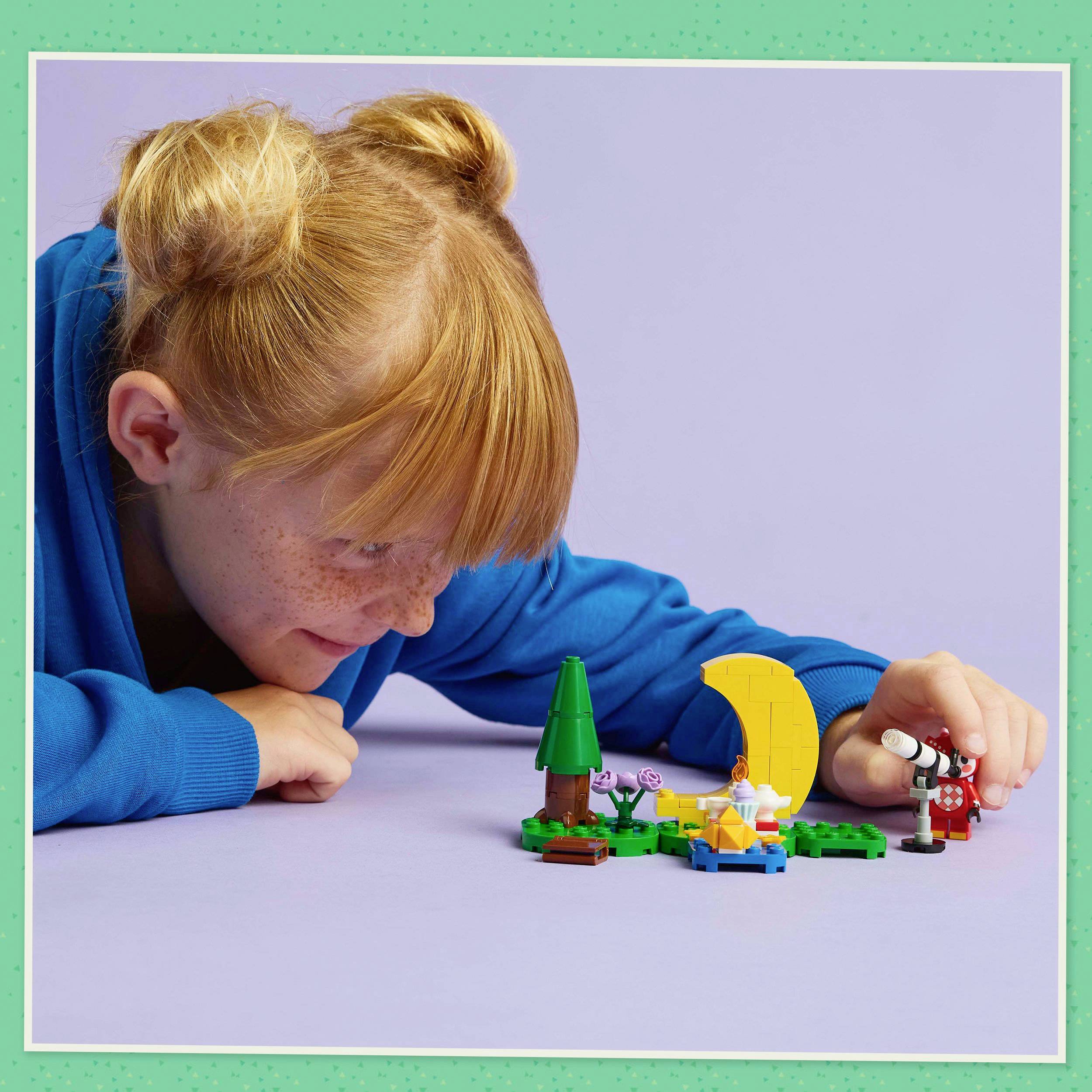 Dziecko z rudymi włosami bawi się figurkami LEGO na stole. Scena przedstawia krajobraz placu zabaw z drzewem i ławką.