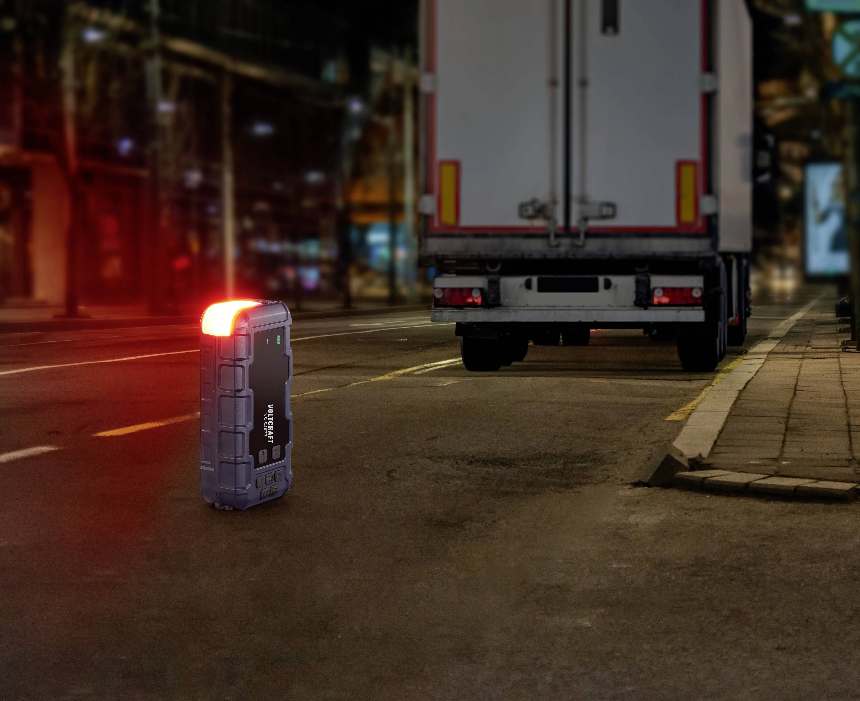 Mały, świecący się kuferek stoi nocą na ulicy przed zaparkowaną ciężarówką. Scena jest miejska i dobrze oświetlona.