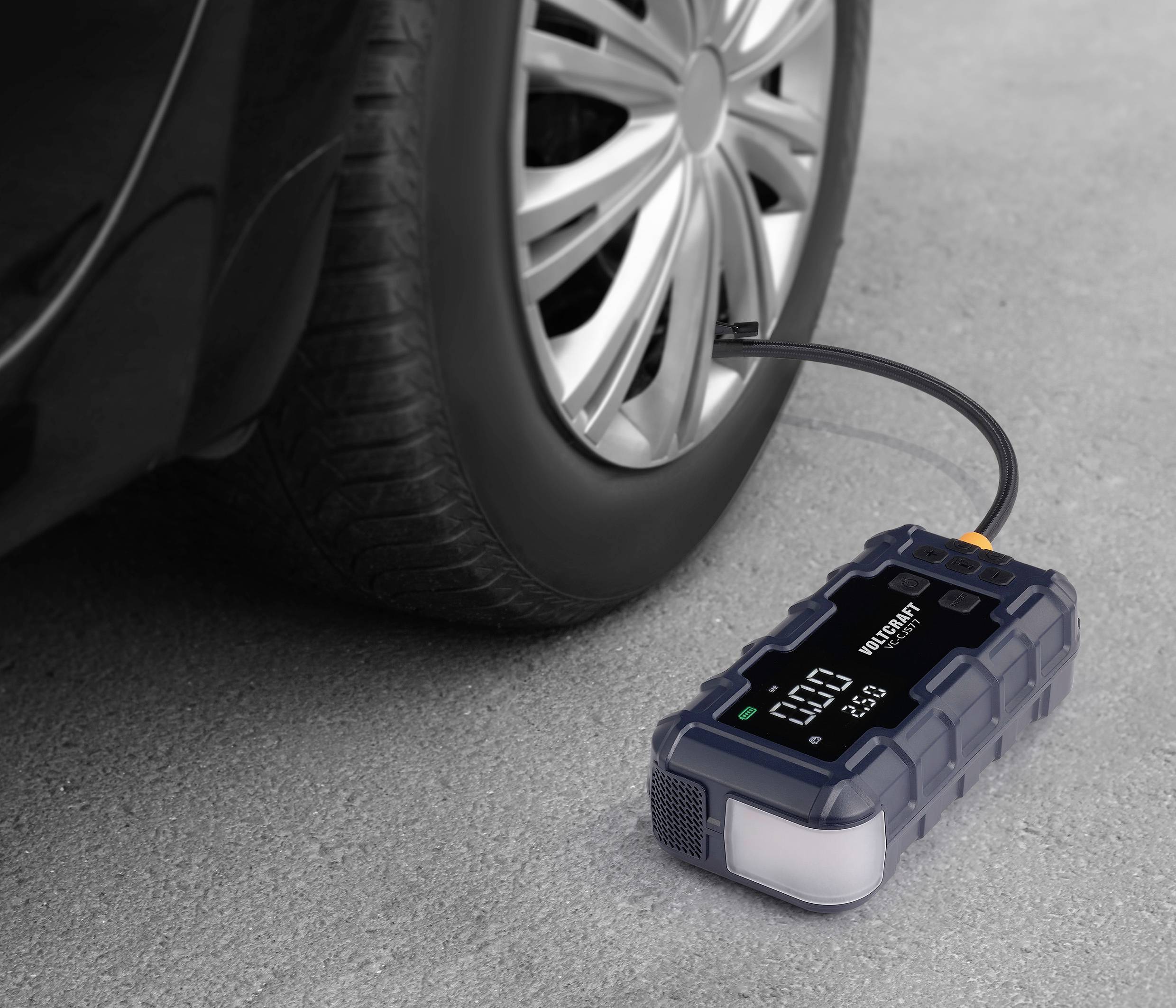 Przenośny, cyfrowy kompresor do opon pompuje opony samochodowe. Wyświetlacz LCD wskazuje ciśnienie w barach. Przewód przyłączeniowy jest zamocowany.