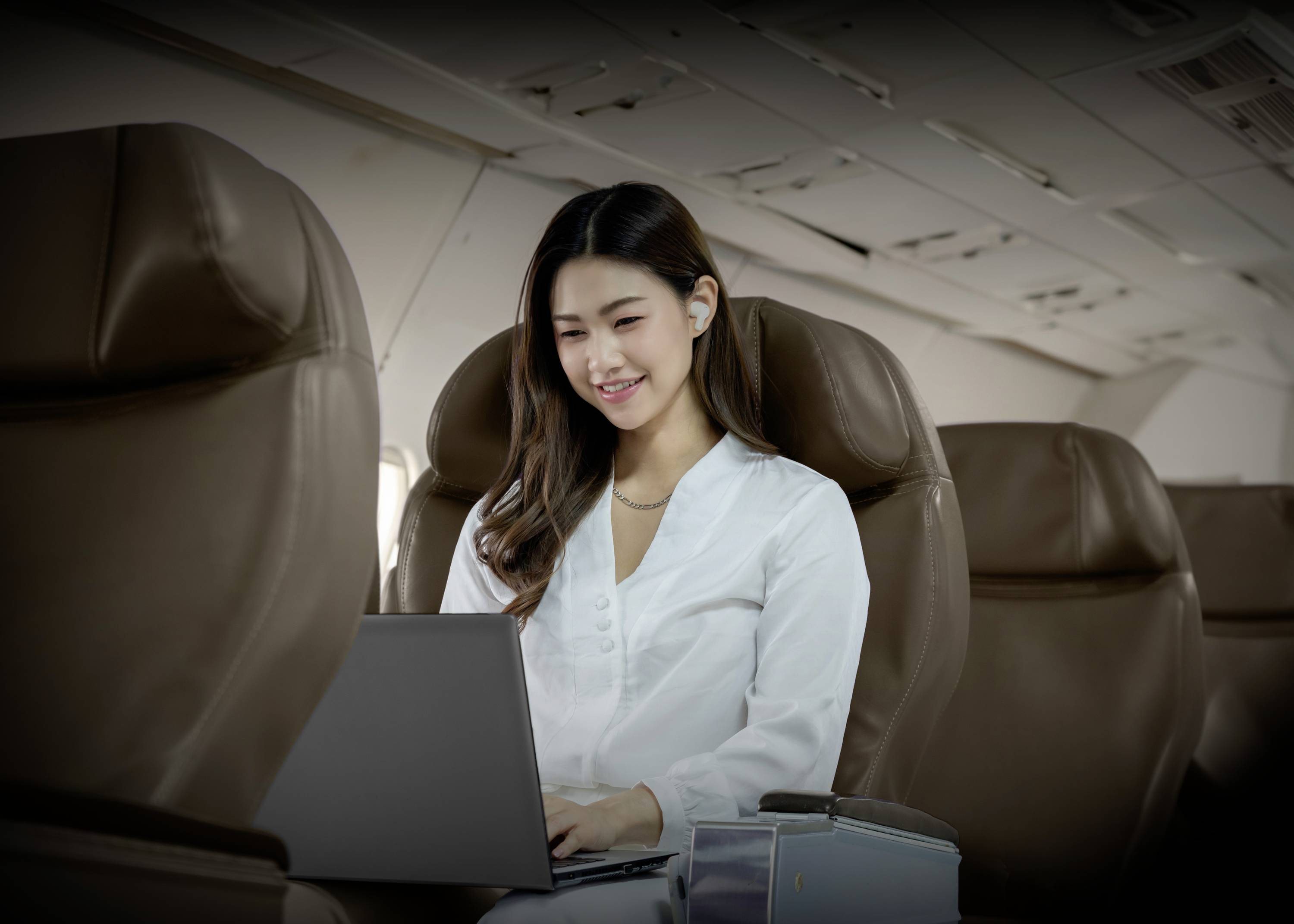 Kobieta pracuje na laptopie w pustym samolocie, ubrana w białe ubranie, skupiona na ekranie.