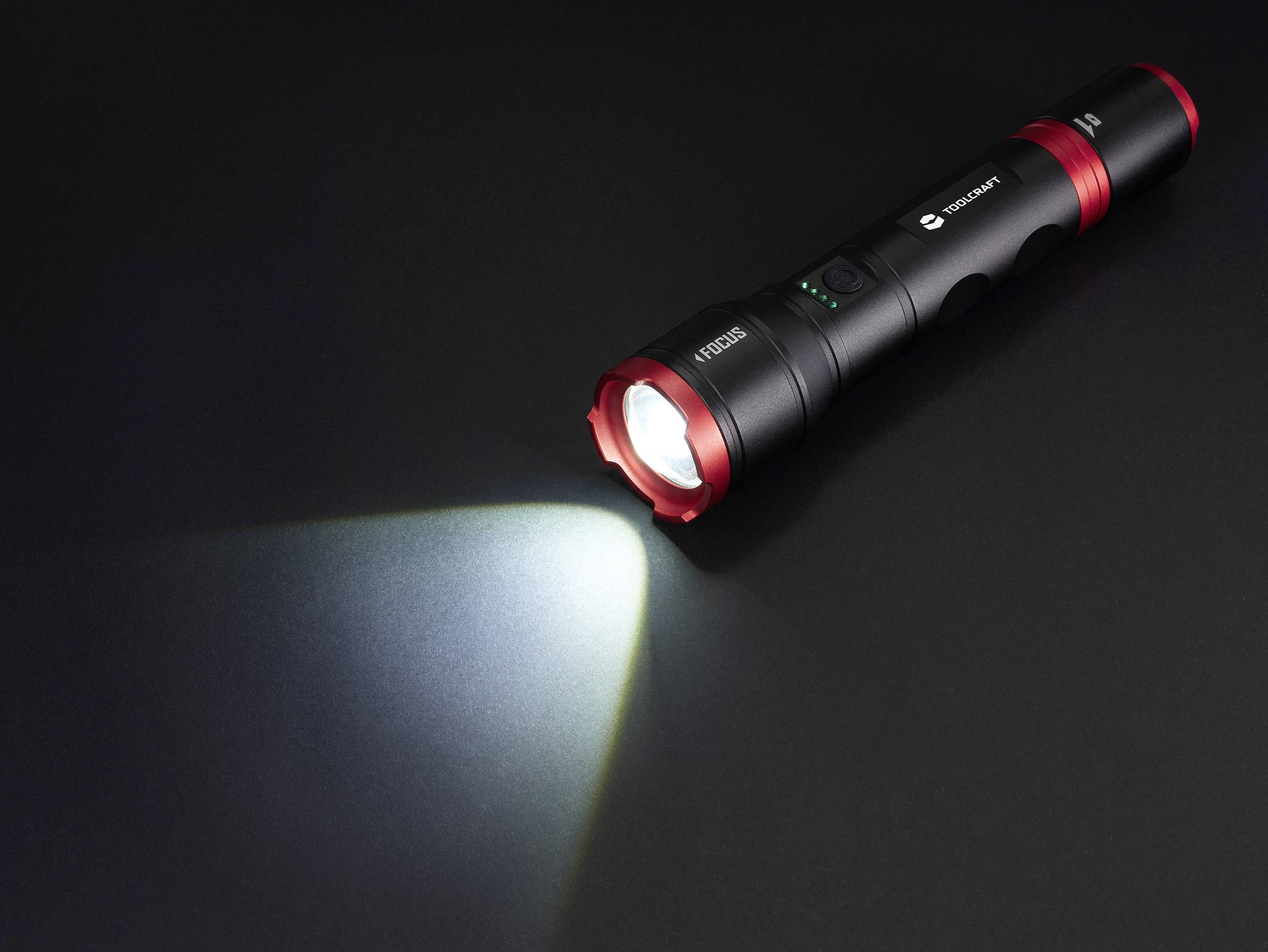 Latarka świeci na czarnym tle, kierując skupiony snop światła w lewą stronę.