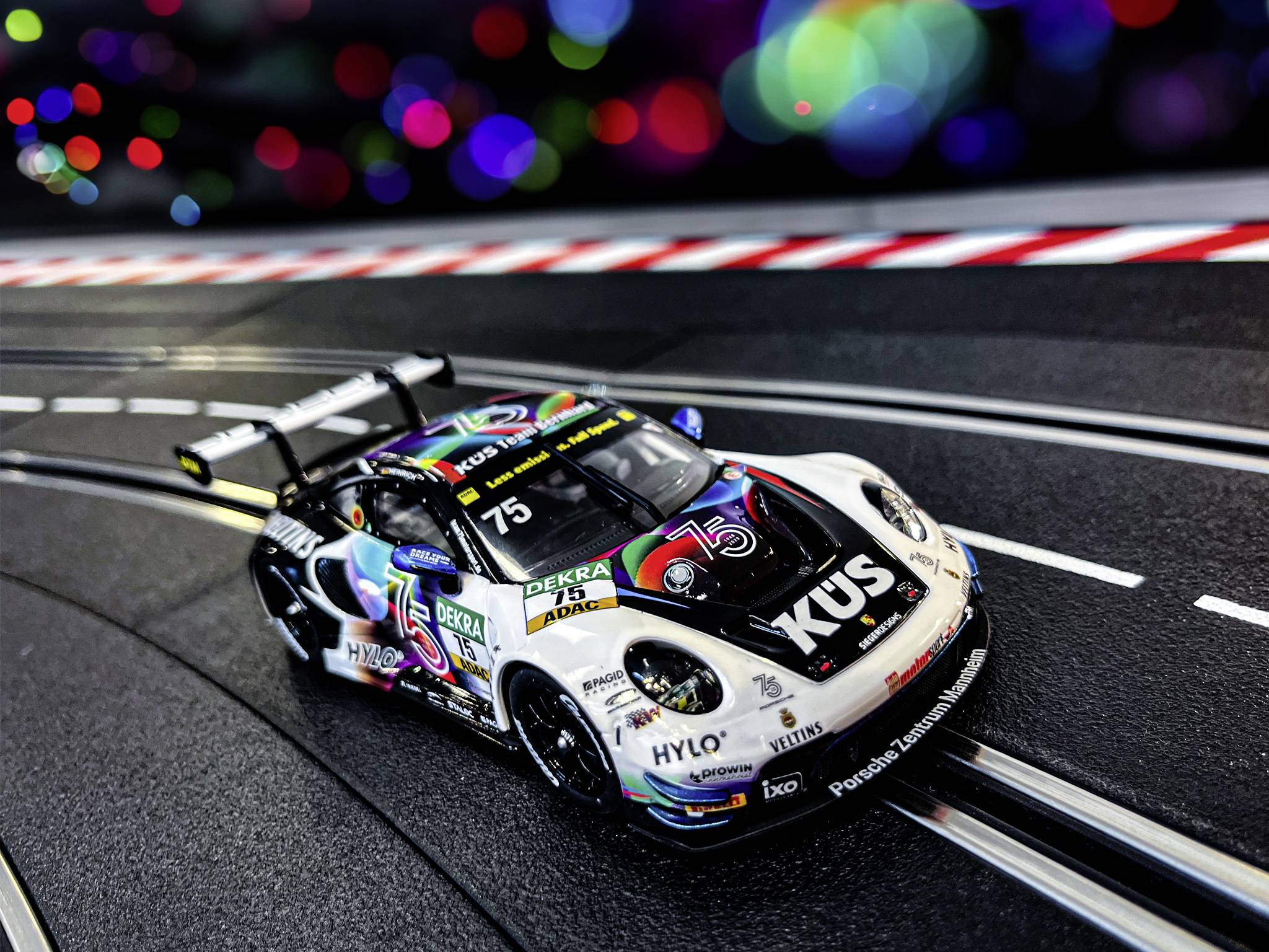 Samochód wyścigowy na torze Carrera z kolorowym oświetleniem w tle. Samochód posiada numer 75 oraz logo sponsorów.