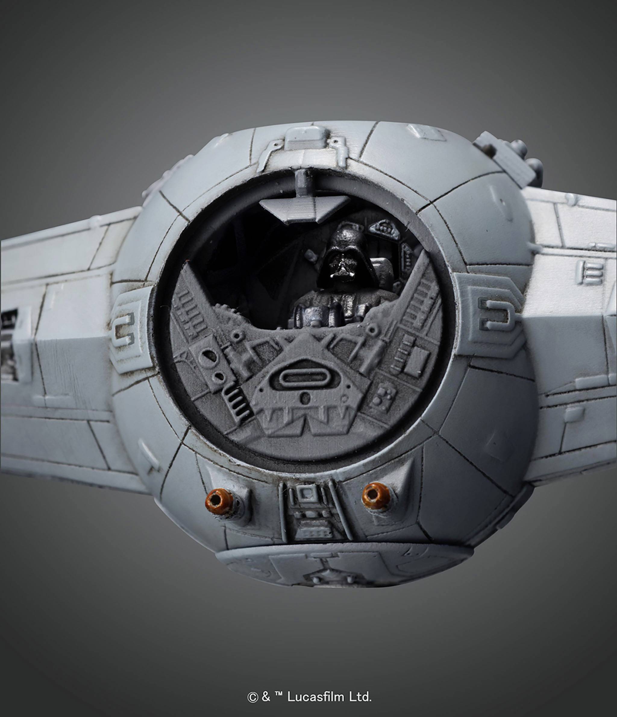 Szary statek kosmiczny z okrągłą kabiną pilota, wewnątrz której znajduje się czarna postać w hełmie. Tło jest ciemnoszare.