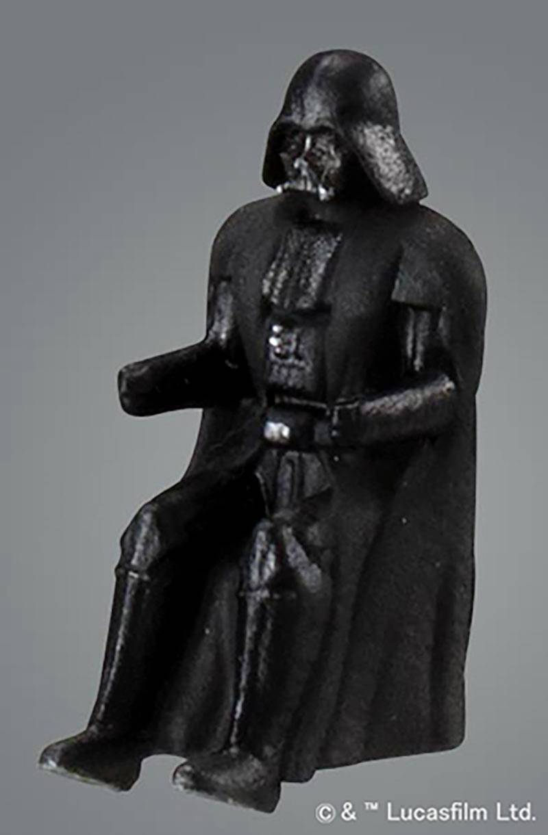 Czarna plastikowa figurka osoby w hełmie i płaszczu, siedząca w pozycji wyprostowanej.