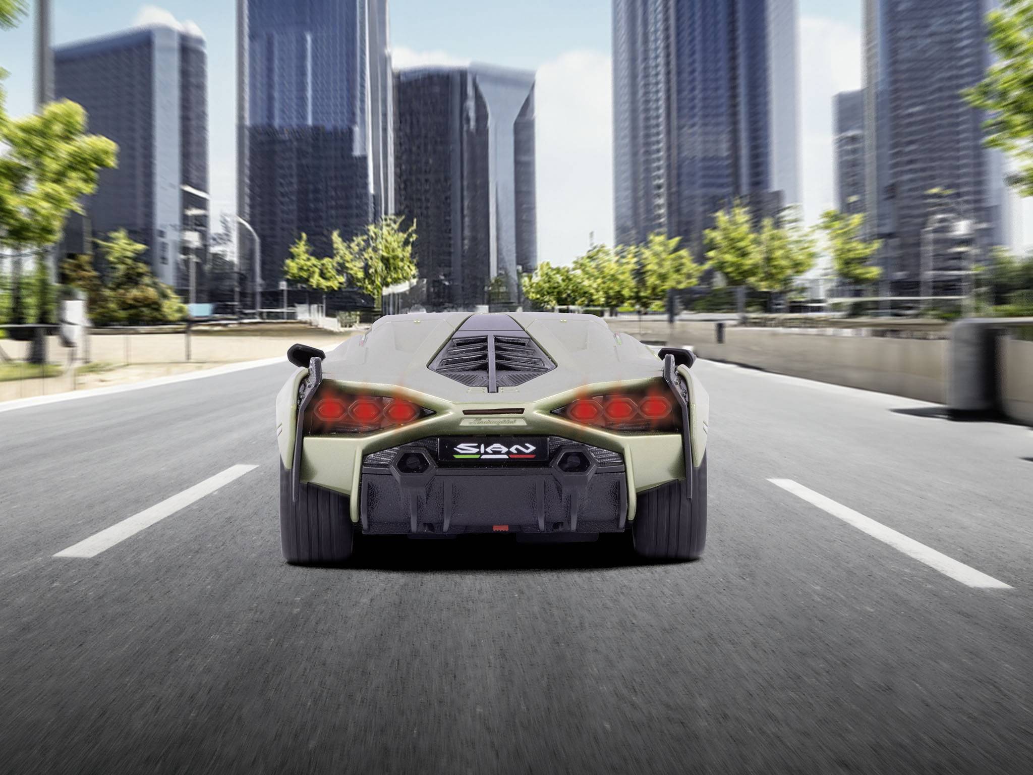 Sportowy samochód jedzie pustą ulicą otoczoną wieżowcami. Wzdłuż drogi rosną drzewa, a w tle widać błękitne niebo.