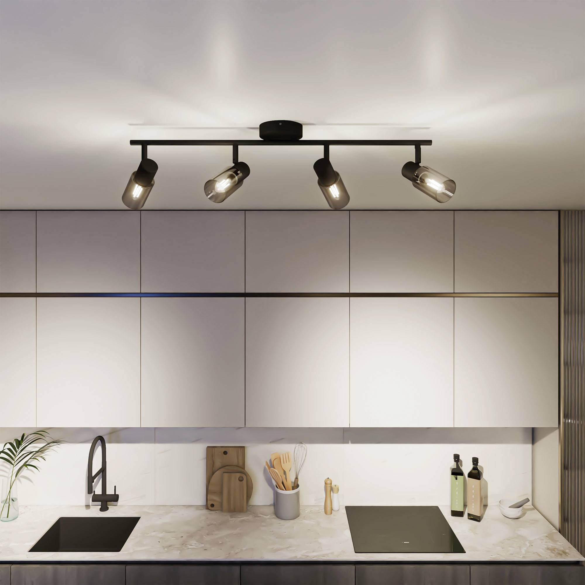 Nowoczesna kuchnia z jasnymi drewnianymi szafkami, czarną baterią i czterema reflektorami na suficie. Po lewej stronie rośliny, a po prawej oleje.