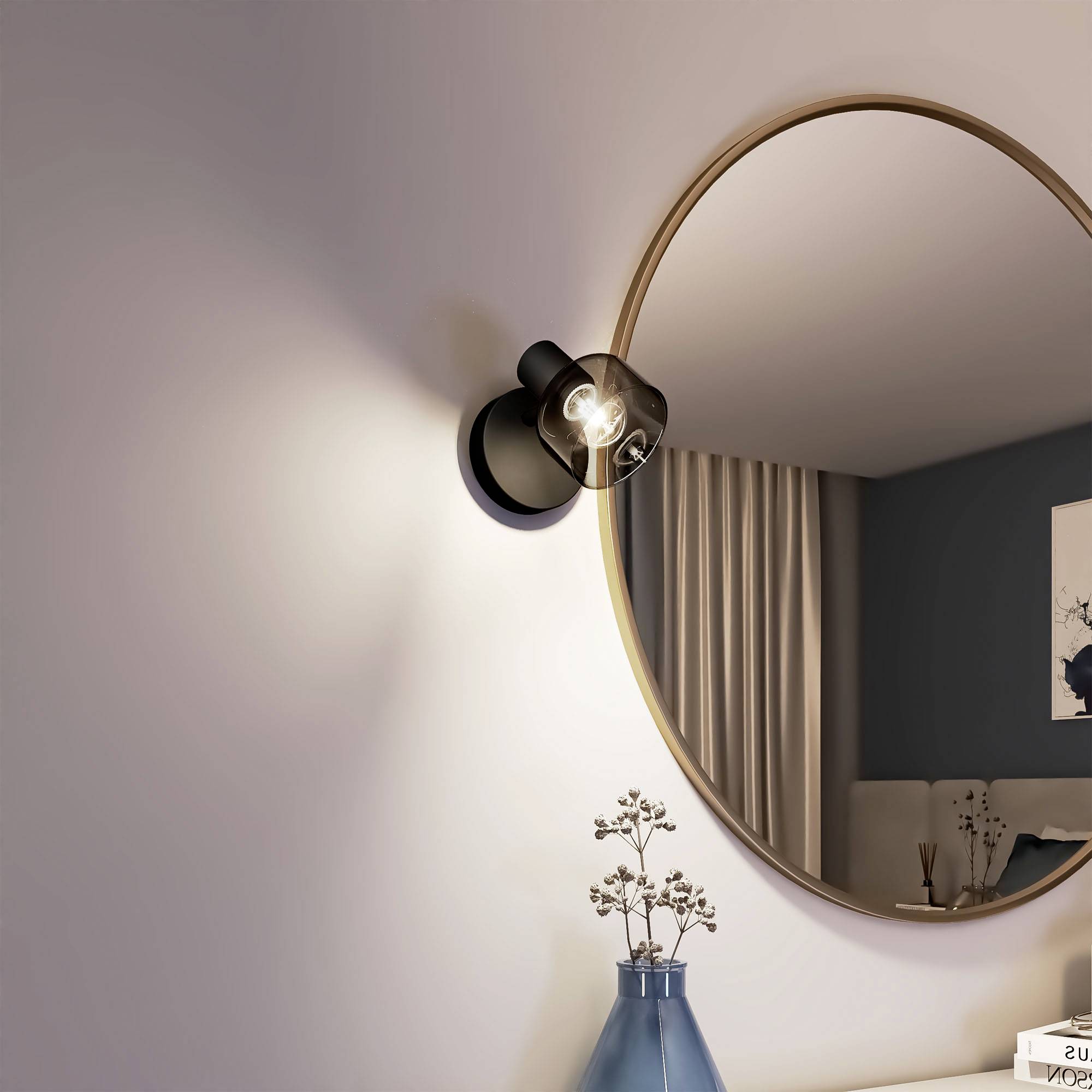 Okrągłe lustro odbija pomieszczenie z zasłonami i dekoracją. Obok znajduje się kinkiet oraz stolik z książkami i wazonem.