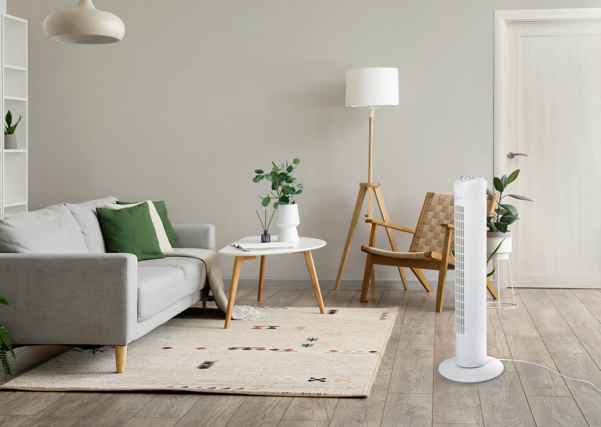 Nowoczesny salon z szarą sofą, zieloną poduszką, białym stolikiem kawowym, lampą stołową z drewna i białym wentylatorem stojącym po prawej stronie.