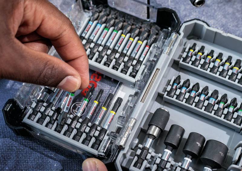 Otwarty przybornik z różnymi bitami i końcówkami. Ręka sięga po jeden bit.