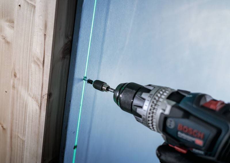 Wiertarka wierci otwór w ścianie. Zielony laser precyzyjnie kieruje wiertłem.