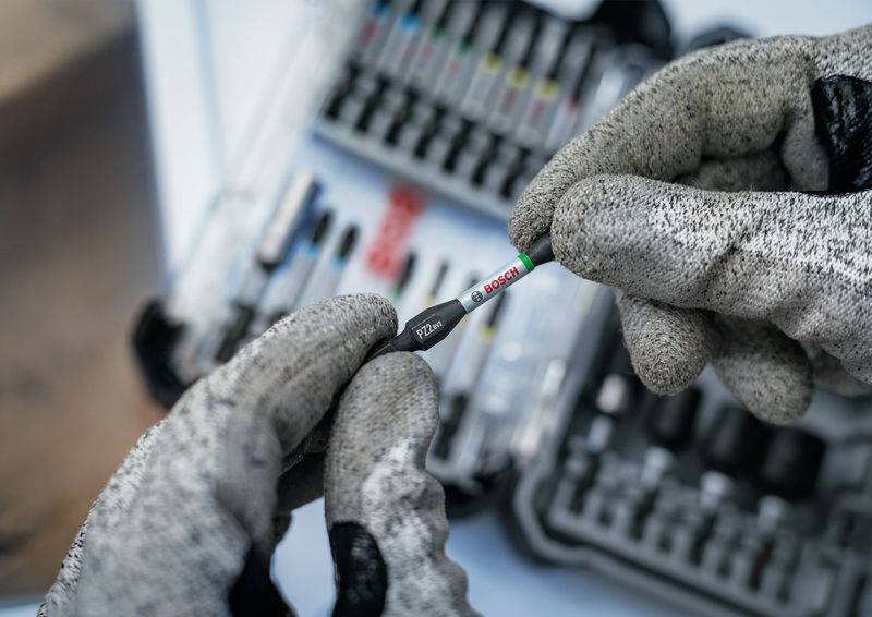 Osoba w szarych rękawicach roboczych trzyma małą pracę przed otwartą skrzynką narzędziową.