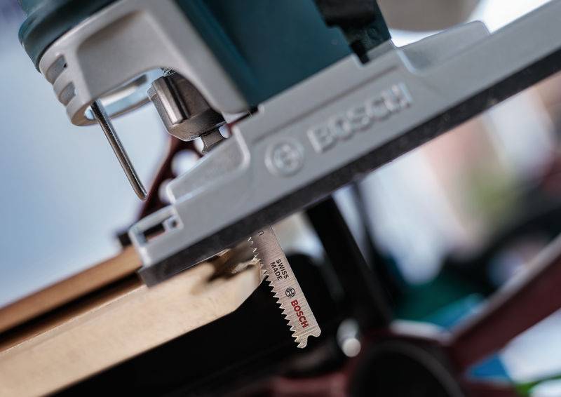 Zbliżenie piły elektrycznej tnącej deskę drewnianą. Szczegółowy widok ostrza piły, z widoczną nazwą marki.