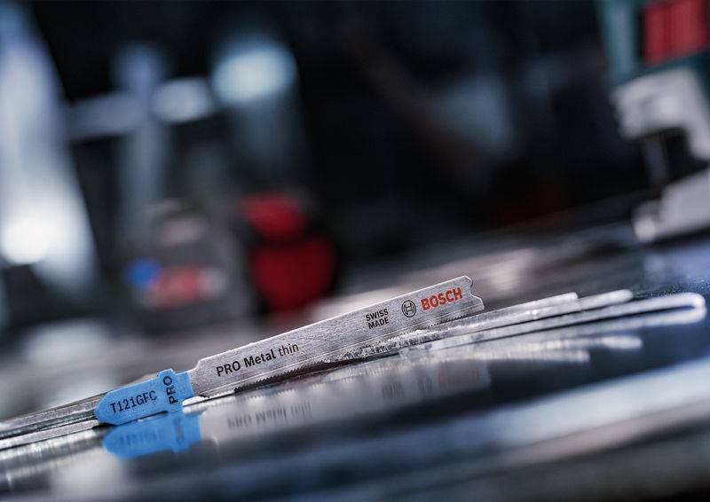 Metalowe ostrze piły z napisem 'PRO Metal thin' leży wyraźnie na rozmazanym tle warsztatowym.