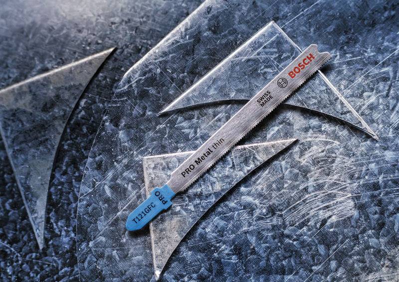 Metalowa powierzchnia z piłą do metalu pośrodku, na której widnieje napis 'BOSCH' i 'PRO Metal'. Ostrze leży skośnie i ma odcień niebiesko-szary.