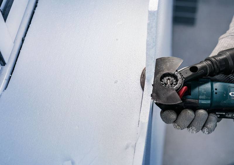 Osoba używa narzędzia elektrycznego do cięcia krawędzi białej, gąbczastej powierzchni.