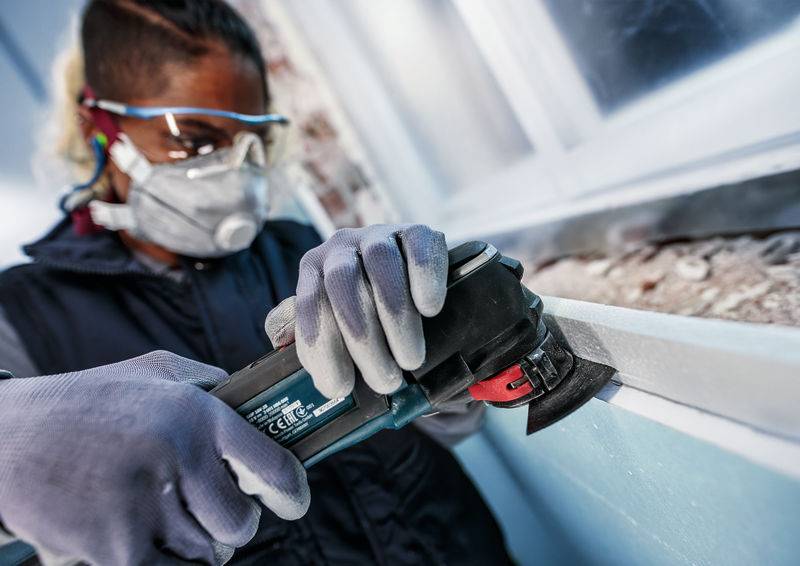 Osoba w okularach ochronnych, masce i rękawicach pracuje szlifierką kątową na powierzchni.