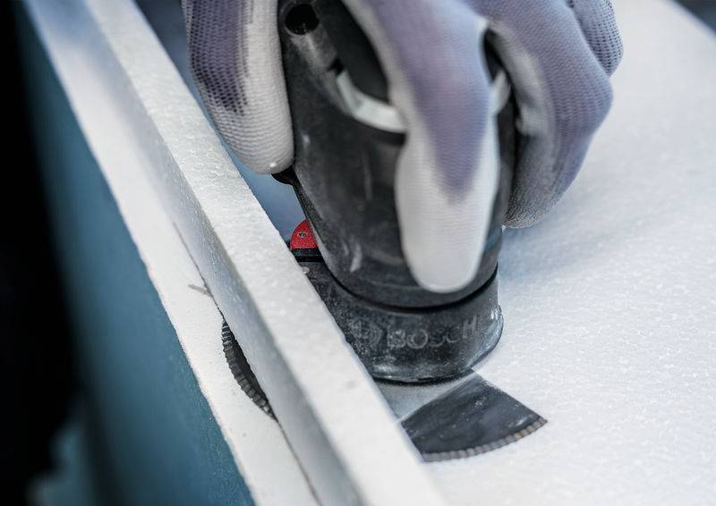 Piła elektryczna przecina białą powierzchnię, podczas gdy osoba jest ubrana w ochronne rękawice.