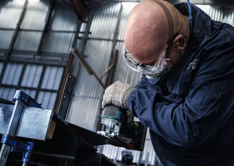 Mężczyzna nosi okulary ochronne i słuchawki ochronne podczas obrabiania metalu szlifierką w warsztacie.