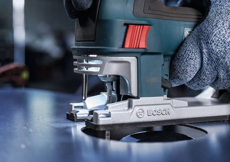 Wyrzynarka wycina okrągły otwór w blasze metalowej. Dłoń w rękawicy mocno trzyma narzędzie.