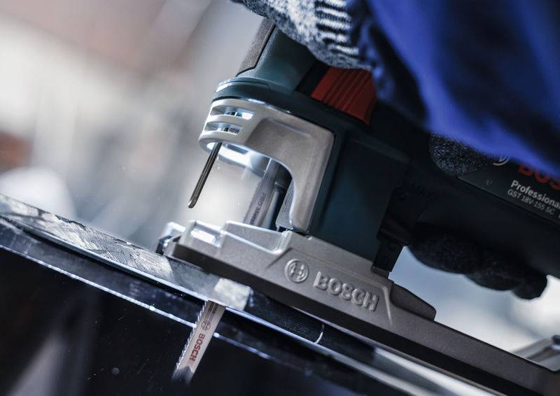 Osoba używa elektrycznej wyrzynarki, aby przeciąć grube materiały. Fokus skierowany jest na brzeszczot piły i precyzję cięcia.