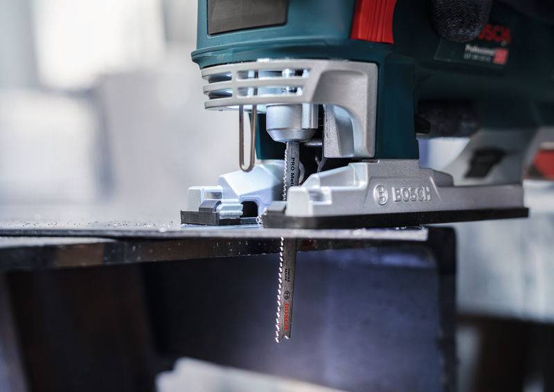 Zbliżenie piły wyrzynarki podczas cięcia kawałka metalu. Piła znajduje się z boku, a proces cięcia jest w toku.