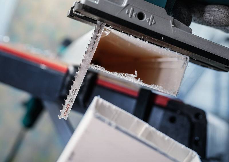 Elektryczna wyrzynarka przecina białą rurę z tworzywa sztucznego. Ostrze piły pokazuje małe wióry z tworzywa sztucznego wzdłuż krawędzi.