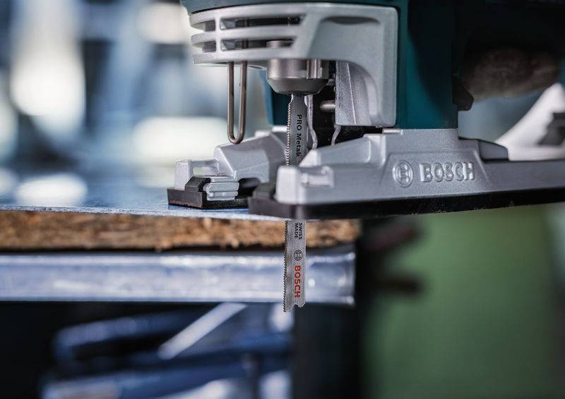 Elektryczna wyrzynarka marki Bosch precyzyjnie przecina kawałek drewna; zbliżenie narzędzia podczas pracy.