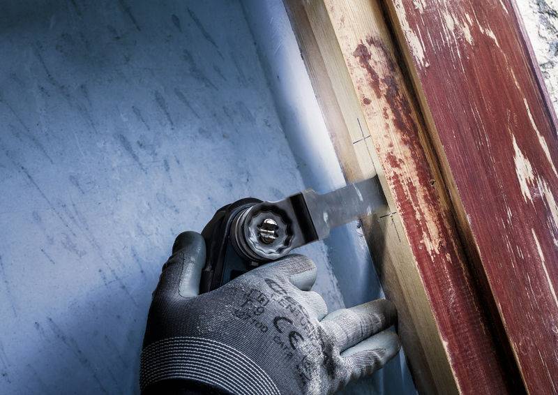 Rzemieślnik w rękawicach przecina piłą drewno przy ramie okiennej.