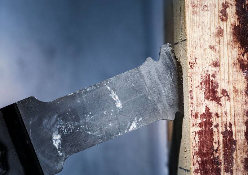 Zbliżenie piły przecinającej deskę drewnianą, wióry drzewne rozrzucone dookoła. Ostrze w centrum uwagi, koncentracja na ostrej krawędzi i jej ruchu.