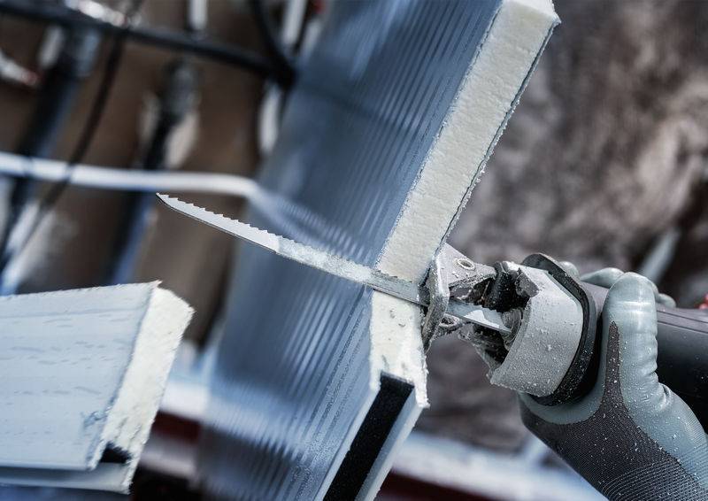 Osoba przycina materiał izolacyjny piłą. Zbliżenie narzędzia i materiału.
