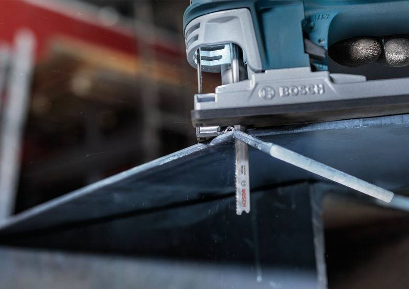 Elektryczna wyrzynarka precyzyjnie tnie arkusz metalu. W tle widać środowisko warsztatu.