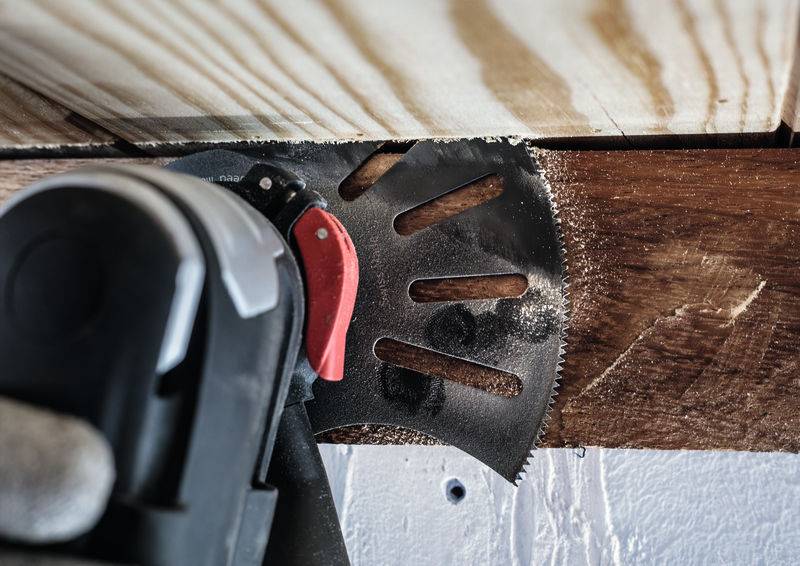 Wielofunkcyjne narzędzie z piłą tnącą przecina deskę drewnianą zamocowaną w ramie.