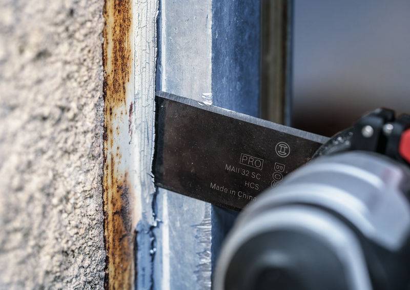 Metalowe narzędzie w zbliżeniu usuwa rdzę z metalowej ramy przy betonowej ścianie.