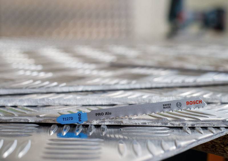 Piła tarczowa z napisem 'PRO Alu' i 'Bosch', leżąca na metalowych płytach o fakturze falistej.