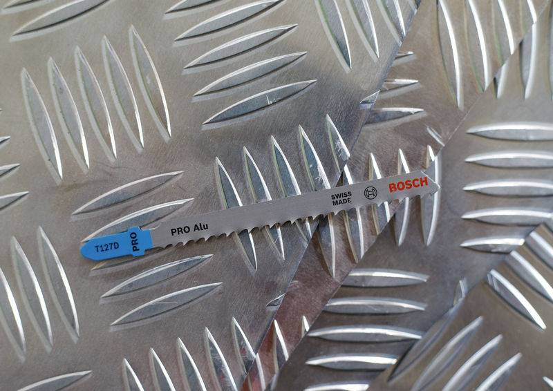 Metalowe ostrze piły z napisami 'Pro Alu', 'Bosch' i 'Swiss Made' spoczywa na ryflowanej metalowej płycie.
