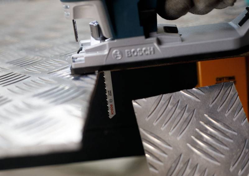 Wyrzynarka przecina arkusz metalu o falistej strukturze. Wykonywany jest rozdzielczy przekrój.