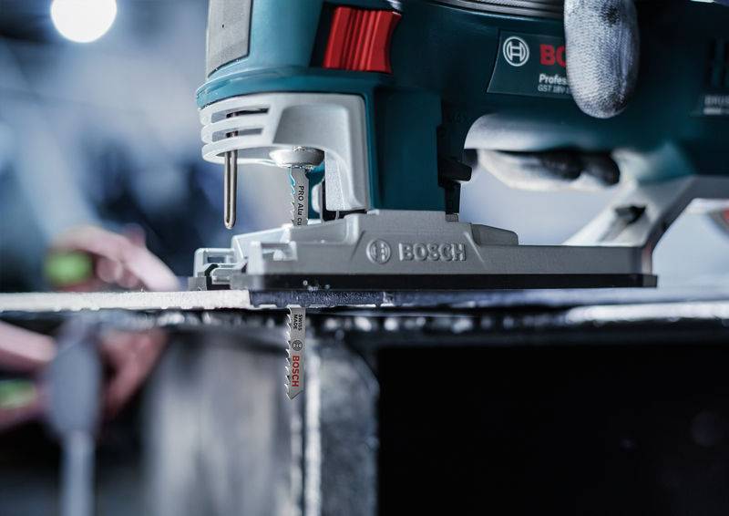 Piła elektryczna przecina kawałek metalu. Widoczne są szczegóły piły i proces cięcia.