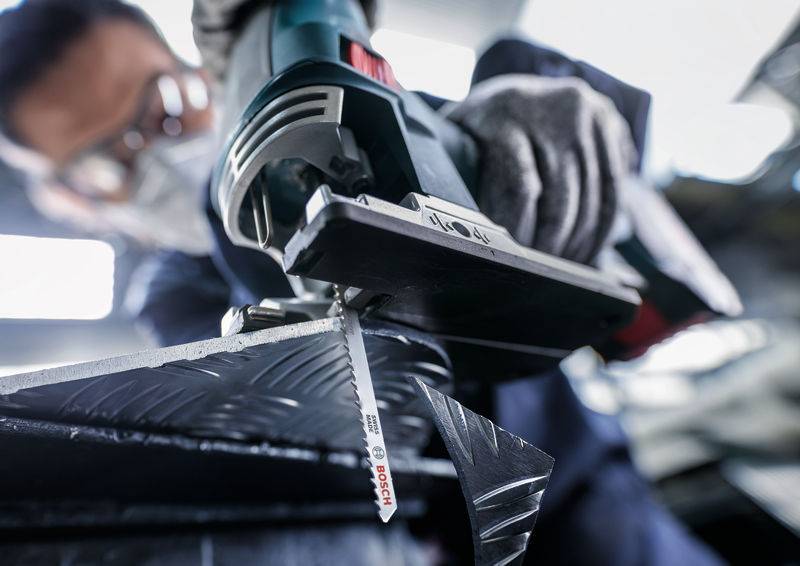 Osoba przecina metal wyrzynarką. Zbliżenie narzędzia i lot iskier. Noszone są okulary ochronne i rękawice.