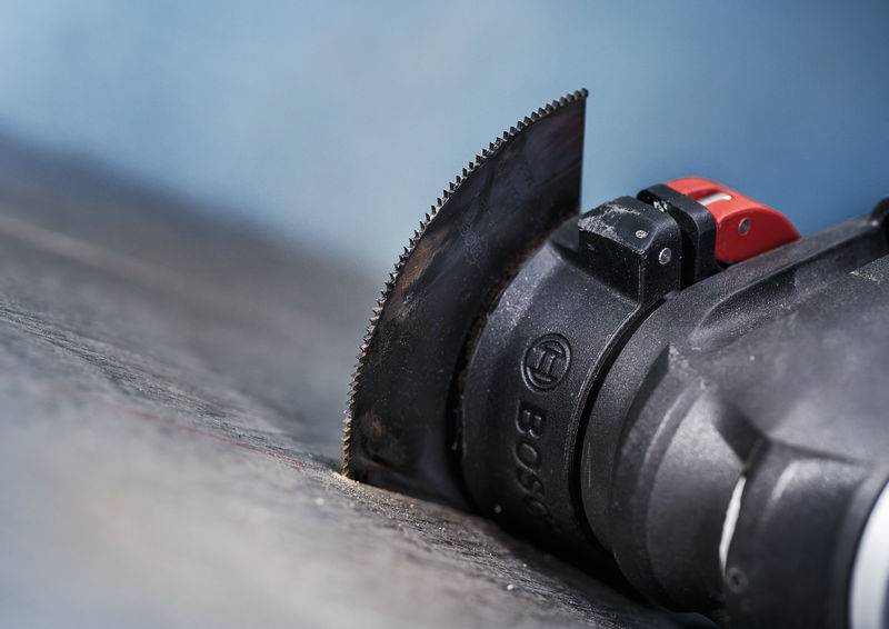 Zbliżenie elektrycznego narzędzia z końcówką tnącą, precyzyjnie wcinającego się w ciemną powierzchnię.