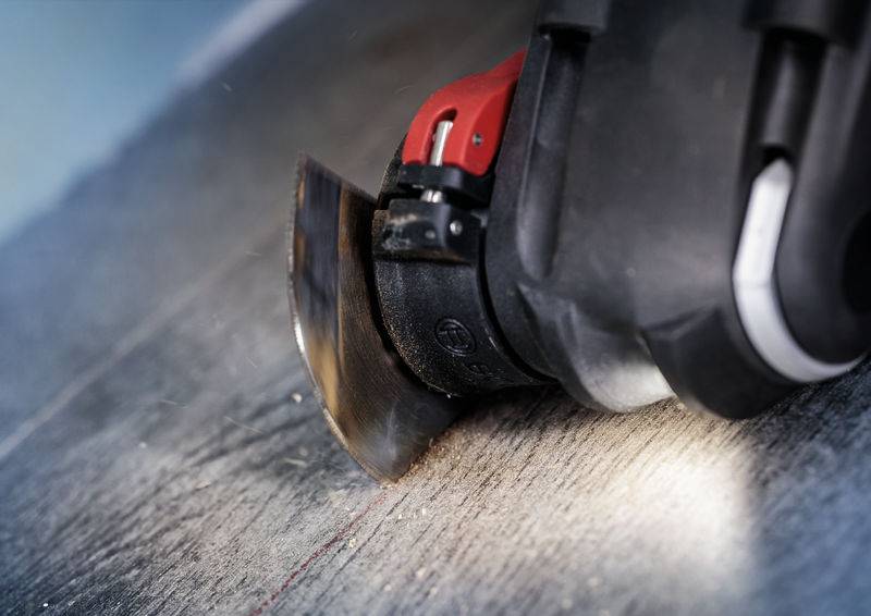 Zbliżenie oscylującego narzędzia z obracającą się tarczą piły, która wycina prostą linię w drewnianym podłożu.