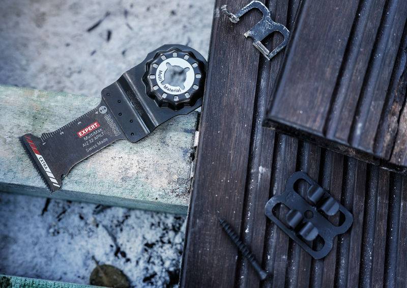 Wielofunkcyjne narzędzie z piłką leży na deskach drewnianych, otoczone śrubami i kawałkami metalu, gotowe do prac rzemieślniczych.