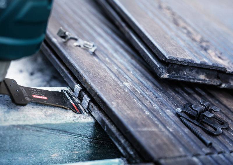 Jedna osoba używa elektronarzędzia do łączenia desek drewnianych za pomocą metalowych zacisków. Nacisk położony jest na połączeniu materiałów.