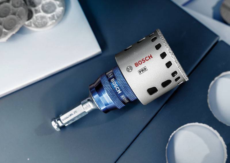 Diamentowa korona wiertnicza firmy Bosch z powłoką diamentową leży na niebieskim podłożu, widoczna nazwa produktu 'Pro'. Odpowiednia do precyzyjnego wiercenia.