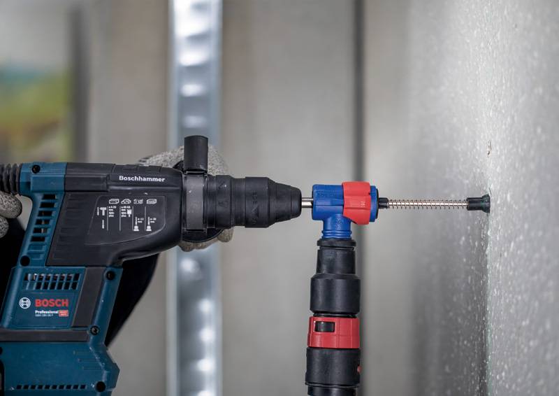 Akumulatorowa wiertarka wierci otwór w ścianie betonowej. Jedna ręka trzyma wiertarkę, podczas gdy wiertło pracuje w ścianie.