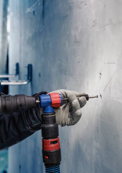 Osoba w rękawicach roboczych wywiera nacisk wiertarką, wykonując otwór w ścianie. Zbliżenie na dłoń i wiertarkę.