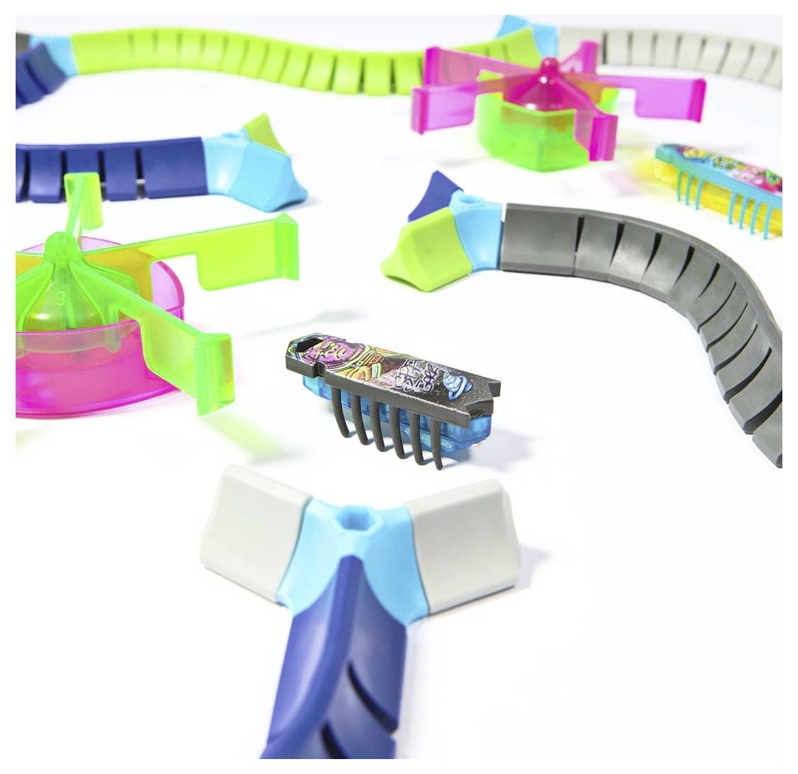 Wielokolorowe, zazębiające się odcinki plastikowego toru z małym, nakręcanym autkiem zabawkowym pośrodku.