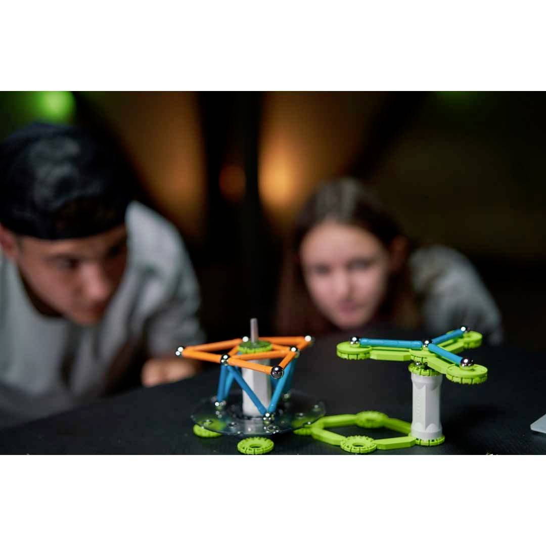 Dzieci przeprowadzają eksperyment naukowy z kolorowymi figurami geometrycznymi, patrząc na obiekty z dużym skupieniem.