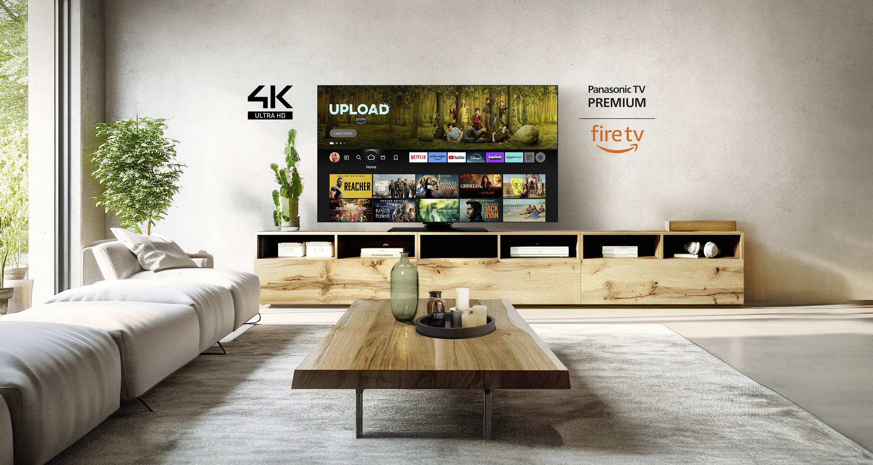 Nowoczesny salon z dużym telewizorem strumieniującym 'UPLOAD'. Po lewej stronie kanapa i stolik, na ścianie logo: 4K, Panasonic, Fire TV.