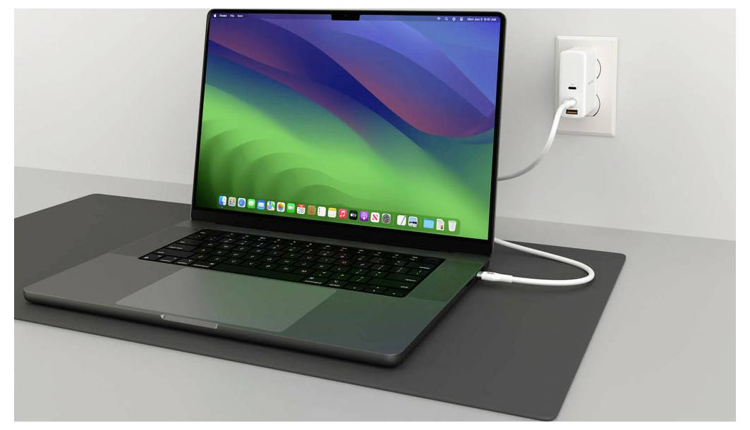 Laptop z kolorowym ekranem stoi na biurku i jest podłączony białym przewodem do gniazdka elektrycznego.