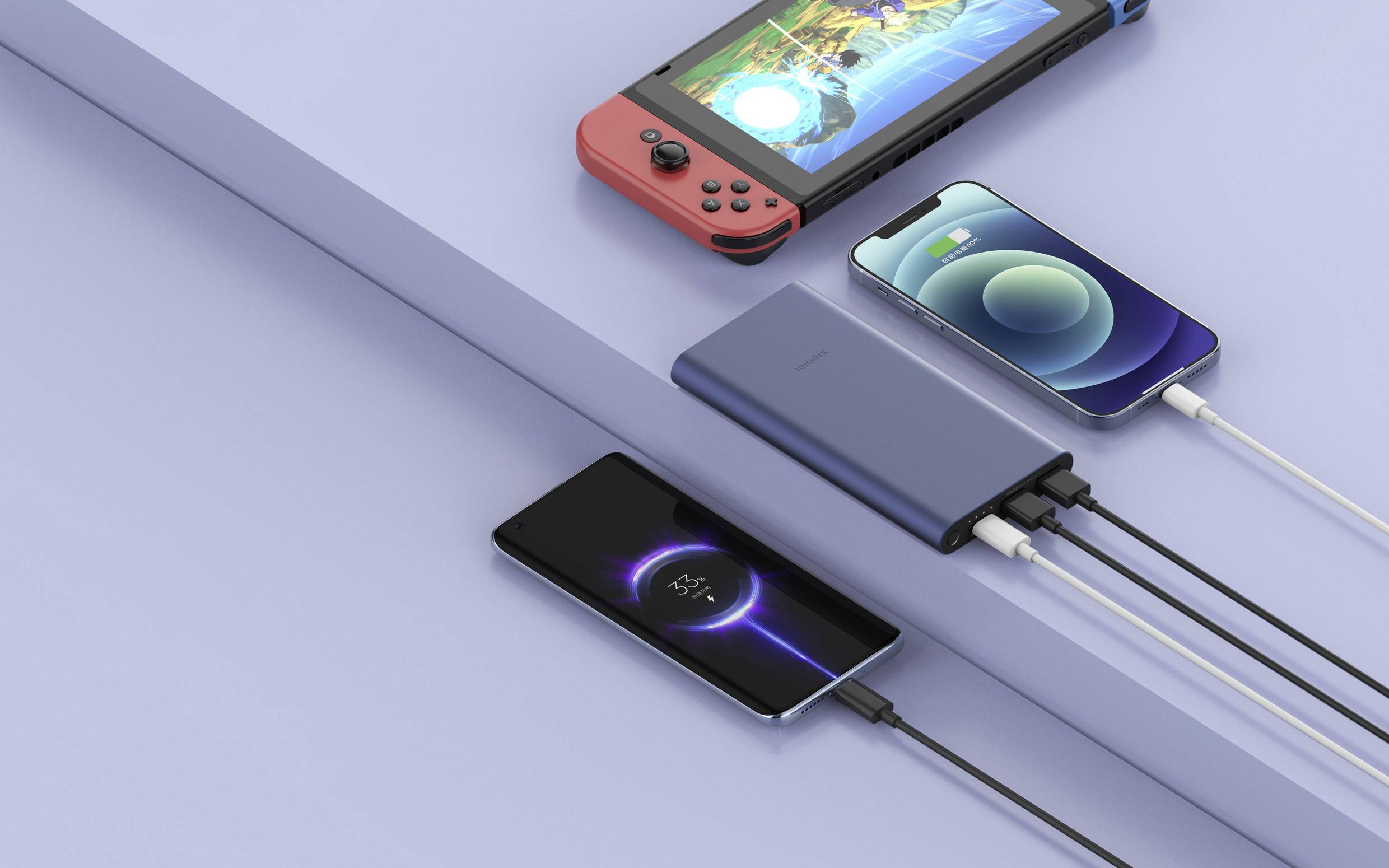 Cztery elektroniczne urządzenia leżą na stole: przenośna konsola do gier, dwa smartfony oraz powerbank ładujący trzy urządzenia.